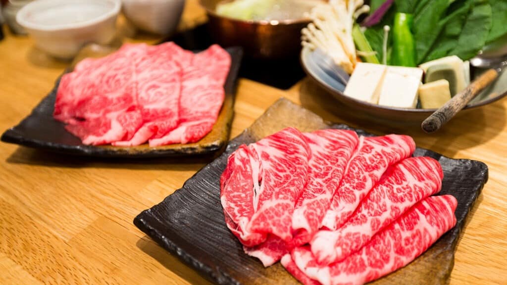 An appetizing array of fresh beef and pork slices prepared for Shabu Shabu and Sukiyaki. The thinly sliced meats exhibit a beautiful marbling, indicative of their high quality and rich flavor. Their vibrant colors contrast against the white plate, promising a flavorful and enjoyable culinary experience.