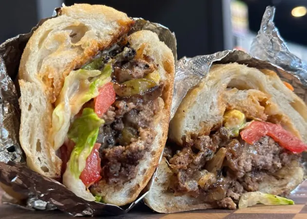 Frazie'S Meat &Amp; Market | Frazie'S Meat &Amp; Market Gourmet sandwich featuring ground beef, fresh lettuce, tomatoes, and pickles, wrapped in foil, highlighting Frazie's Meat & Market's hand-crafted offerings.