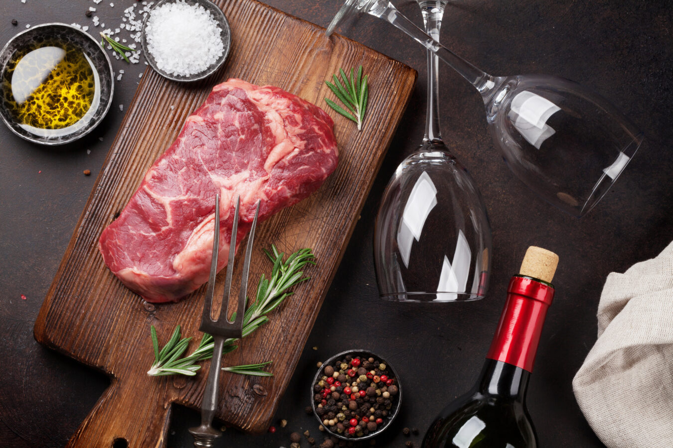 Meat and wine pairing - red wine bottle with wine glasses and steak on a cutting board