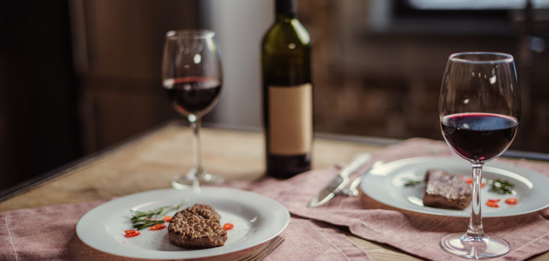 meat and wine pairing - red wine in glass with bottle and two plates with steak