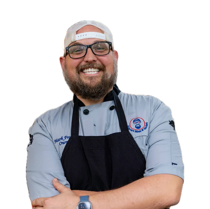 Mark Frazie, owner of Frazie's Meat & Market, in a grey chef's jacket and black apron with his arms crossed.